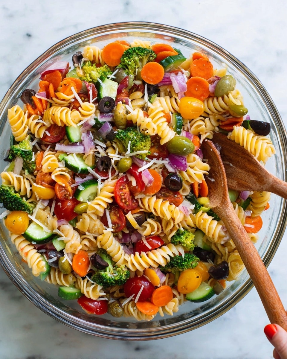 The image shows a clear bowl filled with colorful pasta salad on a white marbled surface. The salad has three layers of spiral pasta in orange, pale yellow, and green colors, mixed with round slices of bright orange carrot, green broccoli florets, chopped yellow bell pepper, slices of dark black olives, small chunks of red onion, thick slices of green cucumber, and red cherry tomato halves. The vegetables and pasta are evenly mixed, and there are small shreds of pale shredded cheese sprinkled on top. Two wooden salad spoons partly dip into the salad from the right side, one spoon being held by a woman's hand. Photo taken with an iphone --ar 4:5 --v 7