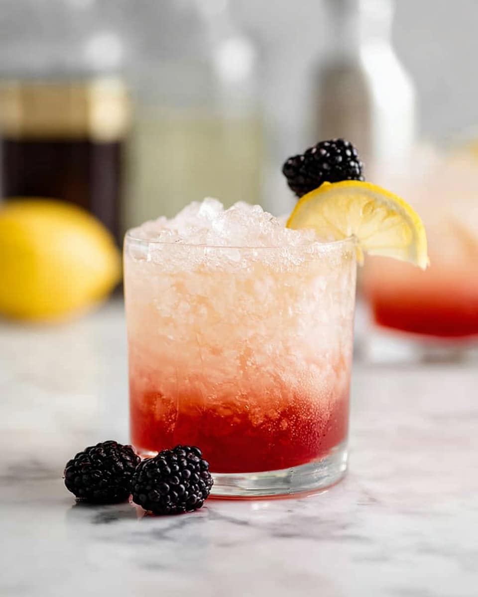 A short clear glass filled with crushed ice and a two-layered drink showing a light pink color on top and a more intense red color at the bottom. The glass is garnished with a thin lemon slice on the rim, with a blackberry placed in front of the lemon slice. Two blackberries rest on the white marbled surface near the glass. In the blurred background, there is another similar glass with the same garnish and some bottles. photo taken with an iphone --ar 4:5 --v 7