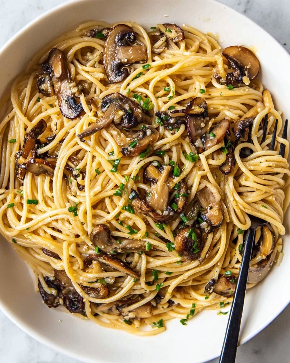 A close-up view of a white bowl filled with light golden spaghetti mixed with sautéed dark brown and tan mushroom slices. The pasta is interspersed with finely chopped green herbs, likely chives, adding small bright green dots on top. The noodles have a glossy, slightly oily texture and are layered in soft curves across the bowl. On the right side, a black fork is stuck into the spaghetti. The bowl sits on a white marbled surface. photo taken with an iphone --ar 4:5 --v 7