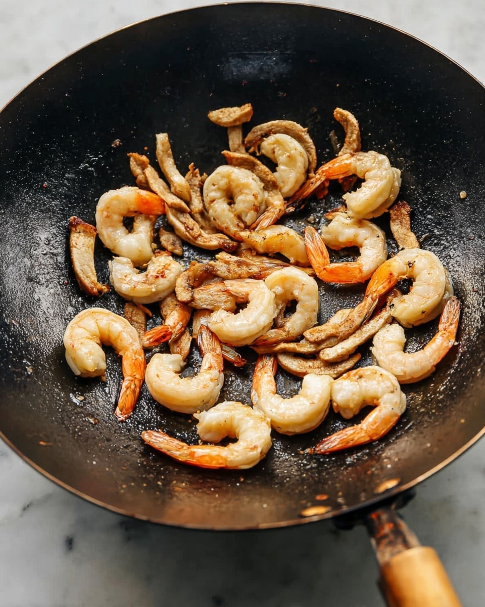 A black wok pan filled with cooked shrimp and strips of chicken, slightly browned and sizzling. The shrimp are a pale pinkish-white color with orange tails, arranged mostly in a circle inside the wok. The chicken strips are light brown with some darker sear marks, scattered among the shrimp. The wok sits on a white marbled surface, and the pan handle with a wooden grip is partially visible on the right side. The lighting highlights the shiny, moist texture of the cooked seafood and chicken. photo taken with an iphone --ar 4:5 --v 7