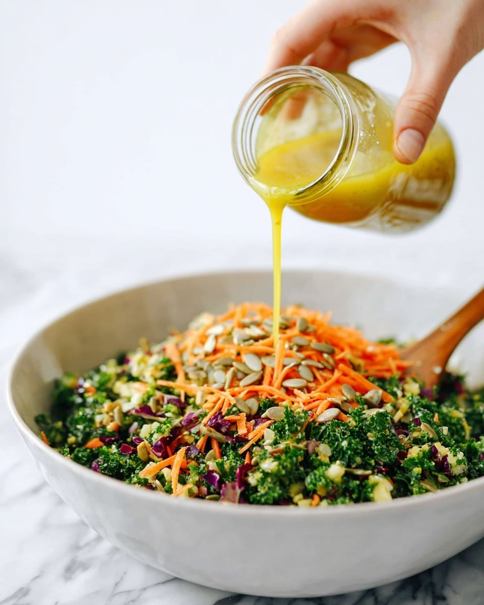 A woman's hand is pouring a yellow dressing from a clear glass jar over a large white bowl filled with a colorful chopped salad. The salad has three visible layers made of finely chopped green kale and broccoli, shredded orange carrots, and small pieces of purple cabbage, all mixed with sunflower seeds scattered on top. There is a light wooden spoon resting inside the bowl. The background is a white marbled texture. photo taken with an iphone --ar 4:5 --v 7