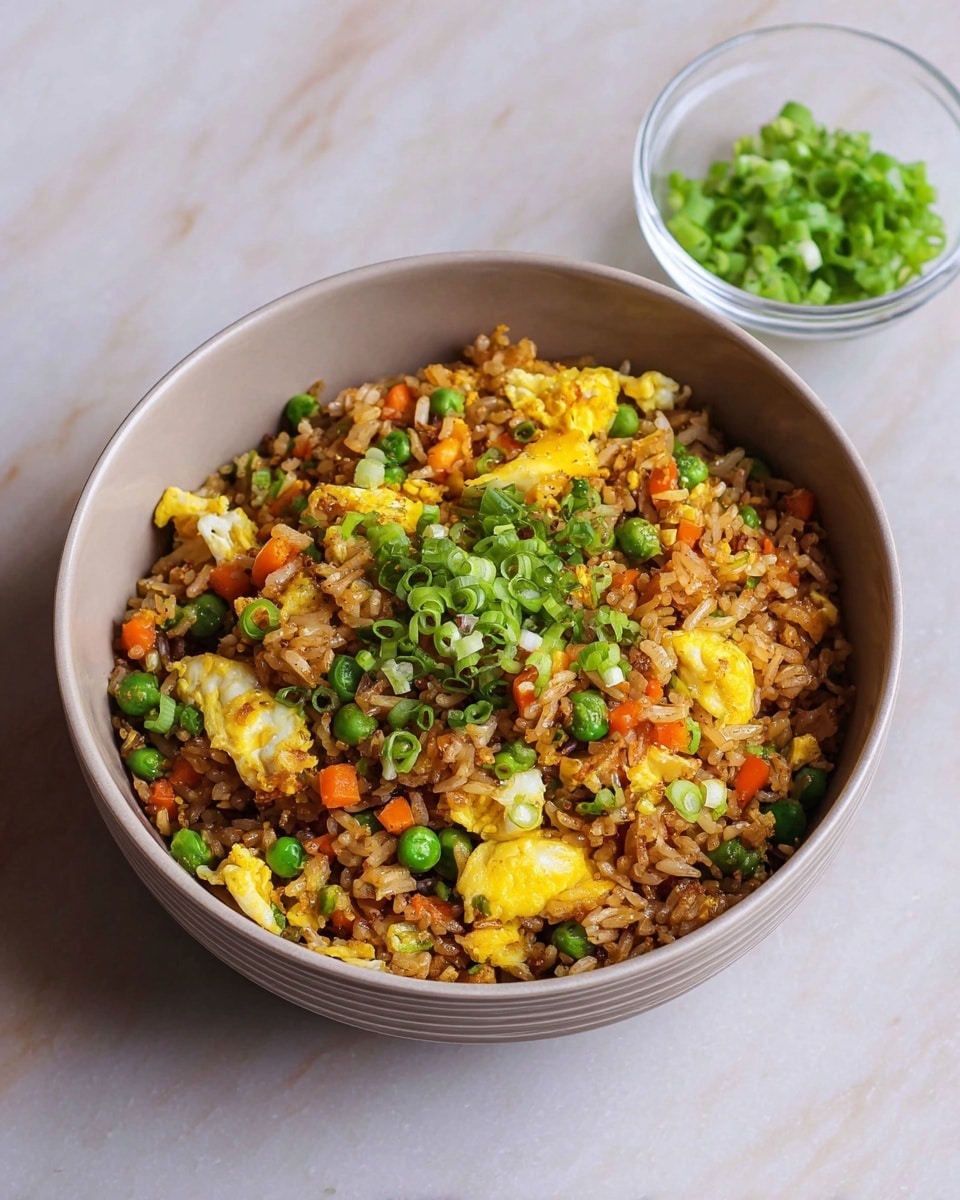 A large white bowl filled with fried rice sits on a white marbled surface, showing three main layers: the brown cooked rice forms the base layer, mixed with small cubes of orange carrots and green peas scattered throughout; the second layer is bright yellow scrambled egg pieces, unevenly spread over the rice; the top layer has small bits of green onion sprinkled all over, adding a fresh contrast to the warm colors; in the upper left corner, there is a small clear glass bowl with more chopped green onions. photo taken with an iphone --ar 4:5 --v 7