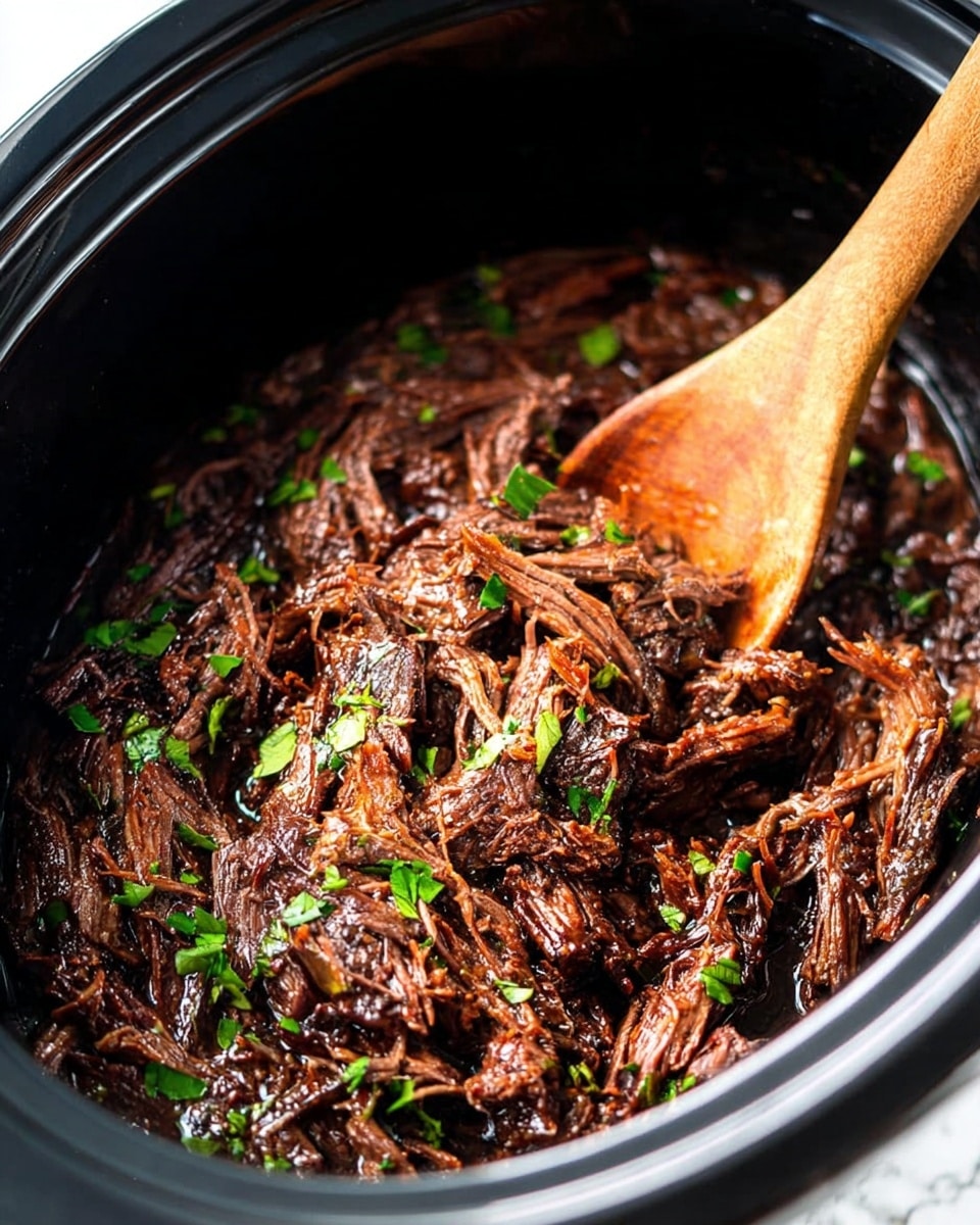 The image shows a close-up view of shredded dark brown meat with a glossy texture, mixed evenly with small chopped green herbs scattered all over. The meat is inside a black slow cooker pot with a smooth inner surface, and a wooden spoon is partially visible on the right side, lifting some meat. The overall look is rich, moist, and tender, with the green herbs adding a touch of fresh color contrast. The background is a white marbled texture photo taken with an iphone --ar 4:5 --v 7