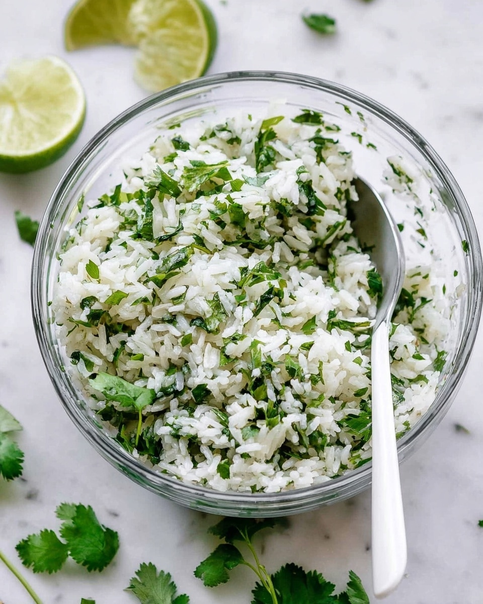 A clear glass bowl filled with white cooked rice mixed with green chopped herbs, mostly cilantro, showing a fresh and light texture. The herbs are mixed evenly throughout the rice, giving a contrast of bright green and white colors. A white spoon is placed inside the bowl, slightly resting on the side. Around the bowl, there are pieces of lime and some fresh cilantro leaves scattered on a white marbled surface, adding a fresh and clean feeling to the image. Photo taken with an iphone --ar 4:5 --v 7