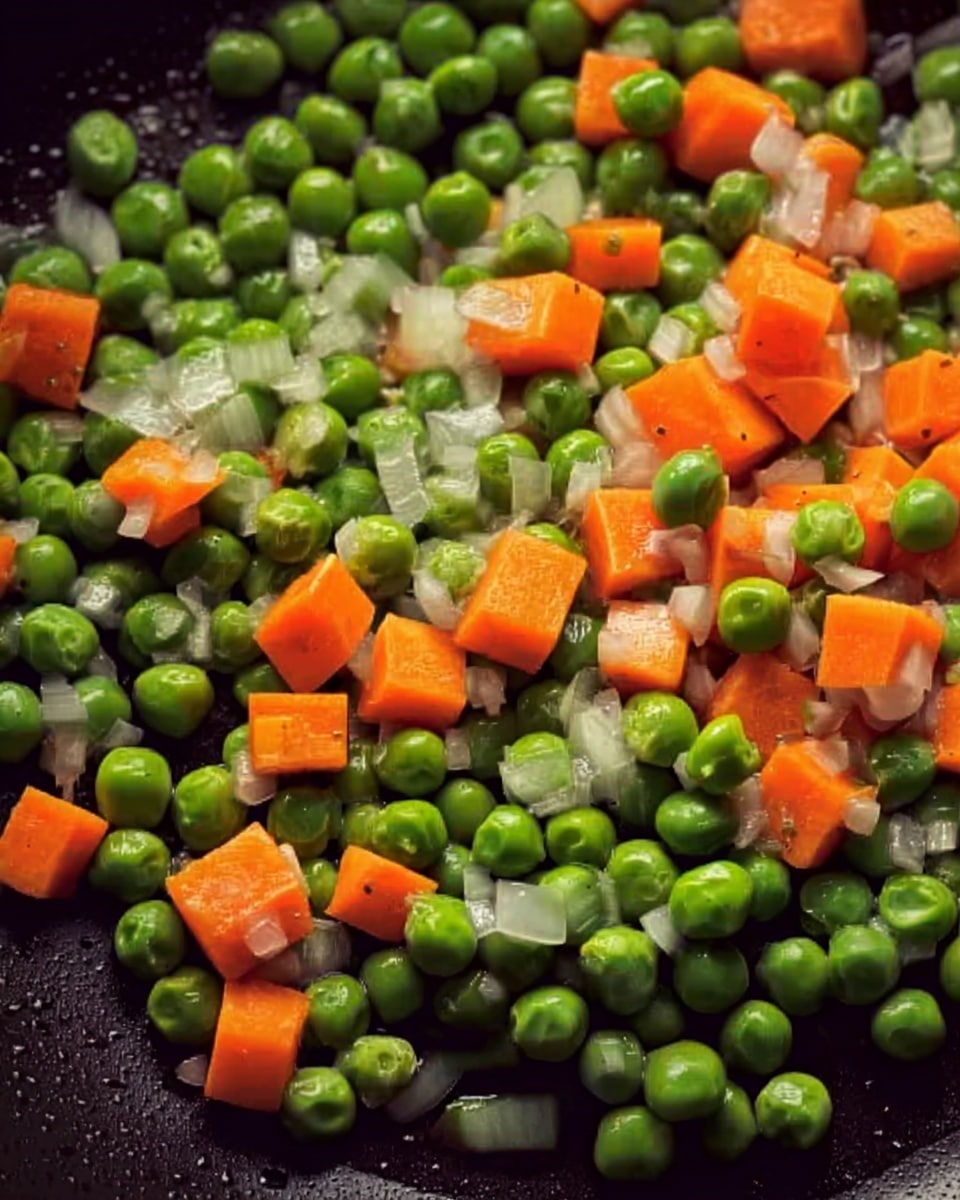 A close-up view of a black pan with bright green peas and small, orange carrot cubes scattered across the surface with tiny white onion bits mixed in, all cooking gently. The vegetables show fresh, smooth textures with a soft shine from heat. The background is a white marbled texture. Photo taken with an iphone --ar 4:5 --v 7
