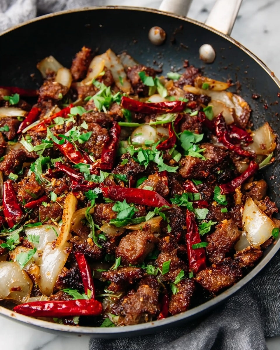 A close-up of a black pan filled with a spicy stir-fry dish that has several layers: the bottom layer is made of browned, crispy pieces of meat scattered evenly; mixed throughout are chunky, translucent white onion pieces with slight caramelization edges; bright red dried chili peppers are spread across, adding pops of color; fresh green chopped herbs are sprinkled on top, adding a fresh contrast; the dish has a textured, glossy look from the sauce coating everything; the pan rests on a white marbled surface with a gray cloth partially visible on the side. photo taken with an iphone --ar 4:5 --v 7