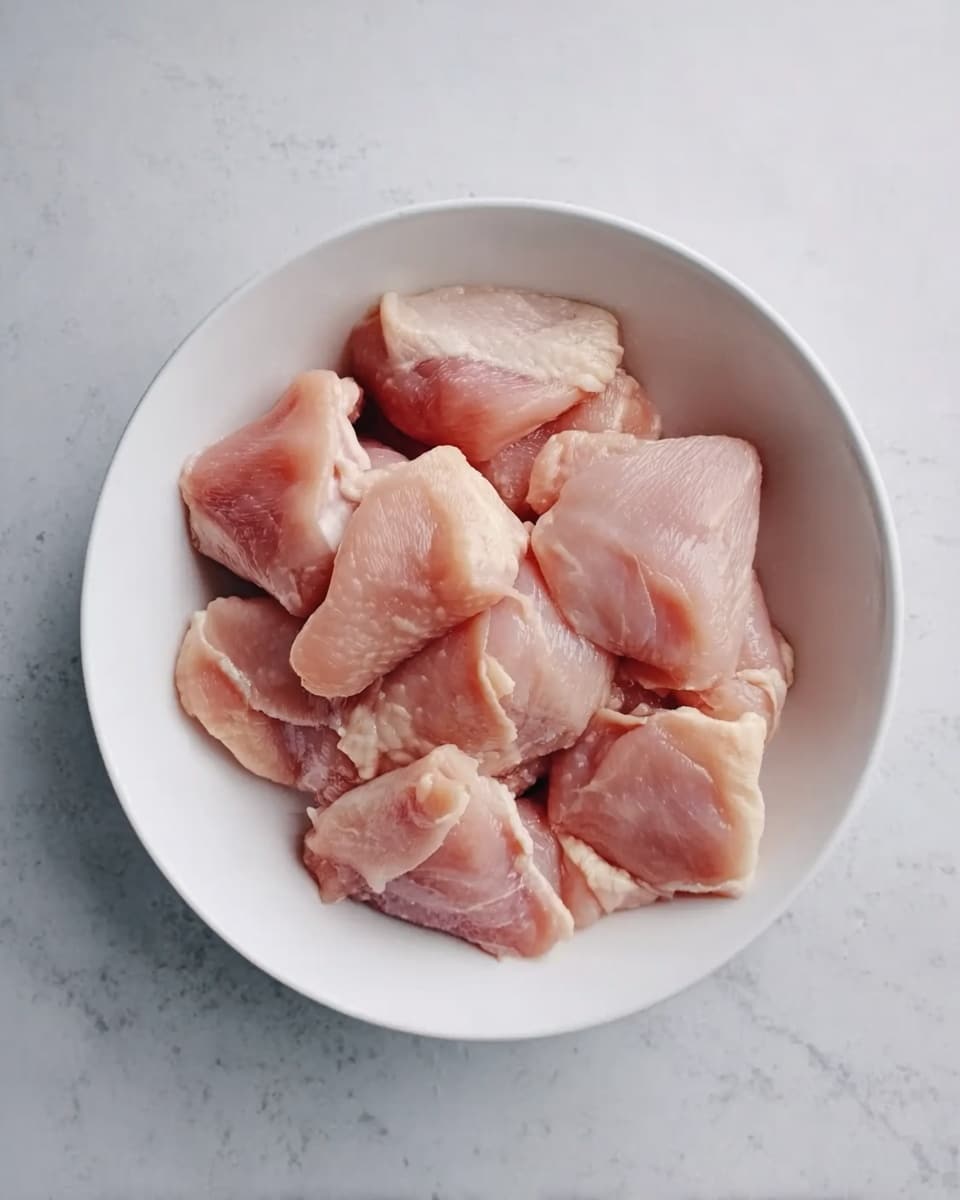 A white bowl filled with several pieces of raw chicken meat, each piece light pink with smooth, slightly shiny skin, placed evenly inside the bowl. The bowl sits on a white marbled surface. Photo taken with an iphone --ar 4:5 --v 7