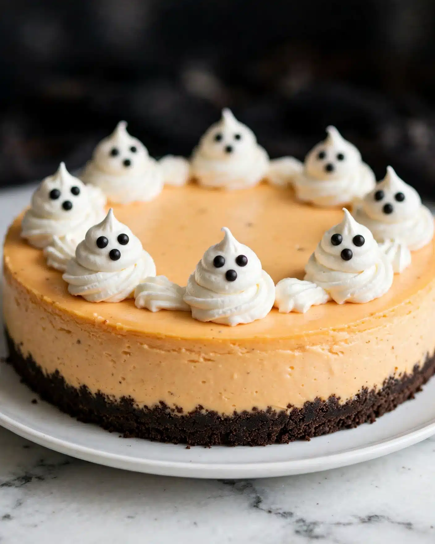 The image shows a round cheesecake with two layers: a dark brown crumbly crust at the bottom and a thick orange creamy layer on top. The cheesecake is decorated with several small swirls of white whipped cream, each topped with two small candy eyes that look like little ghosts. The cheesecake is placed on a white plate set on a white marbled surface, and the photo is taken up close with a dark blurred background, focusing on the front side of the cake. photo taken with an iphone --ar 4:5 --v 7