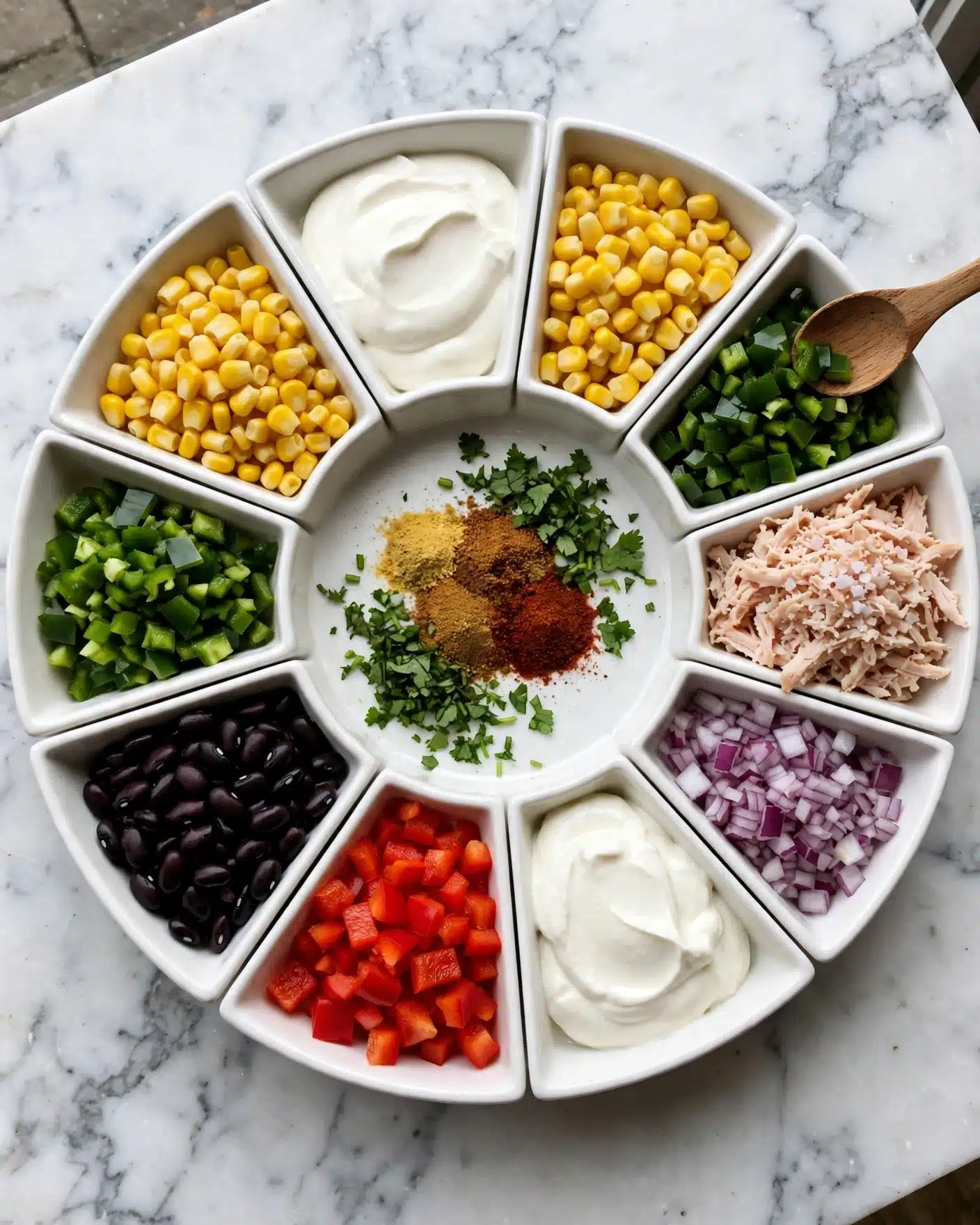 A white bowl with nine different sections of food arranged in a circle. Starting from the top going clockwise, the first section contains smooth, white sour cream. Next to it is bright yellow corn kernels. Then dark green chopped green peppers with a wooden spoon resting on the bowl’s edge. After that, there is light pink shredded chicken with a sprinkle of white salt on top. Next to the chicken, finely diced purple onions are placed. A big dollop of white sour cream sits next to the onions. Bright red chopped bell peppers fill the next section. A pile of shiny, dark black beans is next to the peppers. In the center of the bowl are three spices in small piles: light yellow, brown, and deep red, with chopped fresh green herbs surrounding them. The bowl rests on a white marbled surface. Photo taken with an iphone --ar 4:5 --v 7