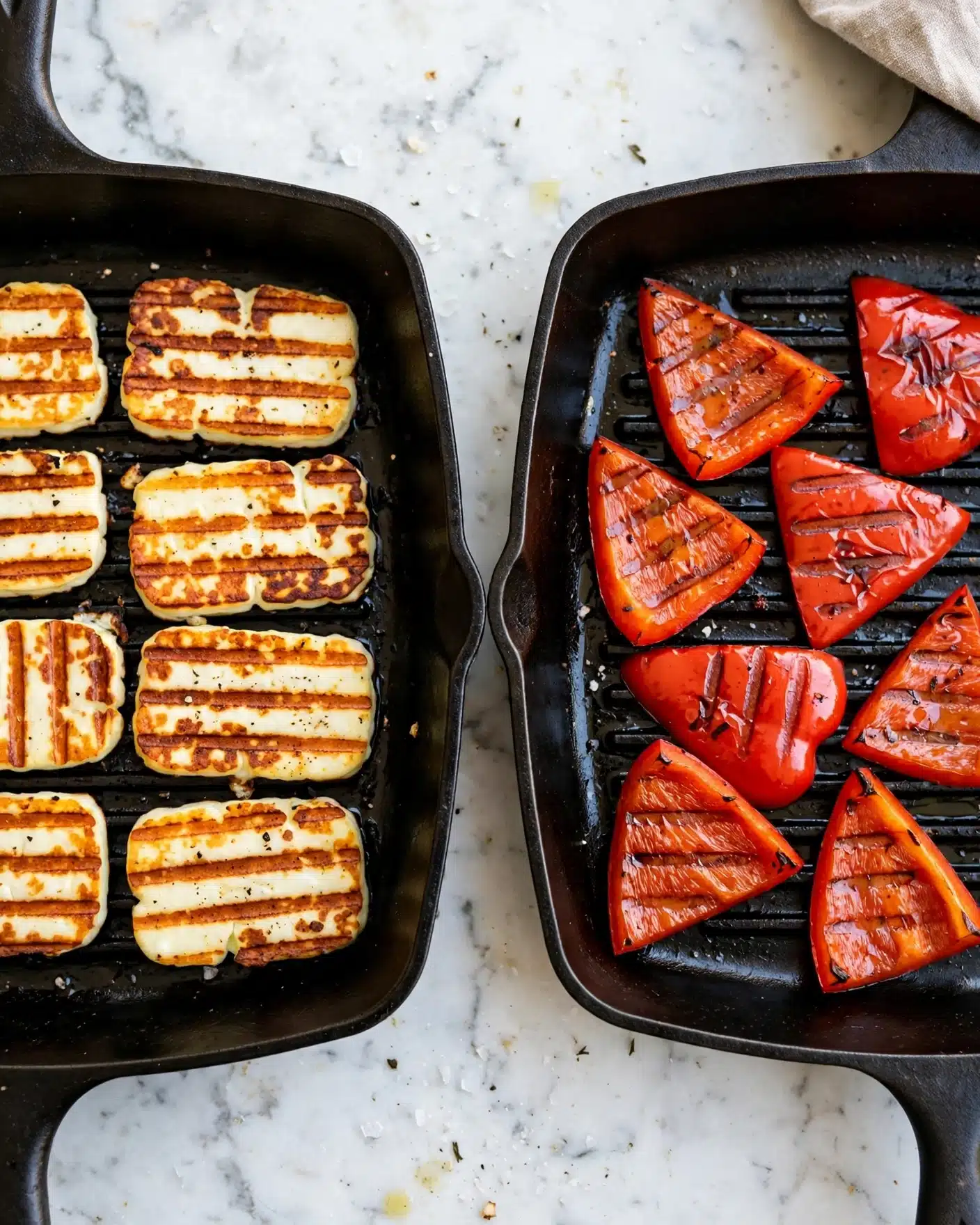 The image shows two black grill pans side by side on a white marbled surface. The left pan has eight pieces of halloumi cheese, each piece rectangular with a creamy white color, marked by strong brown grill lines running horizontally. The cheese pieces have a slightly crispy texture with some showing light browning edges. The right pan contains seven triangular slices of red bell pepper, all brightly colored with deep red skin and clear brown grill marks in a horizontal pattern. The peppers look slightly shiny and tender from grilling. Photo taken with an iphone --ar 4:5 --v 7