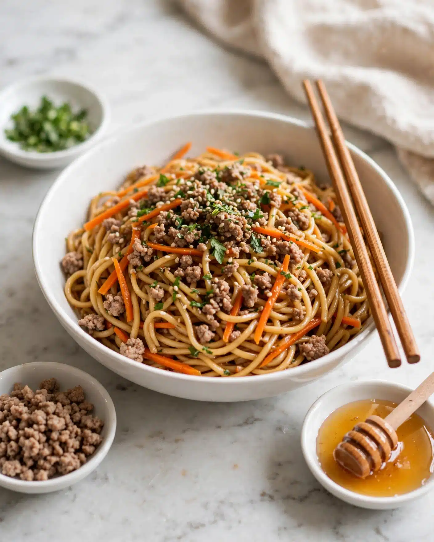 A white bowl filled with twisted, golden-brown noodles mixed with small pieces of cooked light brown minced meat, and thin orange carrot strips evenly spread throughout. On top, the dish is covered with a layer of more browned minced meat sprinkled with chopped green herbs and sesame seeds, adding touches of green and white to the warm colors. Light brown wooden chopsticks rest on the right side of the bowl. Surrounding the bowl are small white dishes containing chopped green herbs, minced meat, and honey with a wooden honey dipper on a white marbled surface. photo taken with an iphone --ar 4:5 --v 7