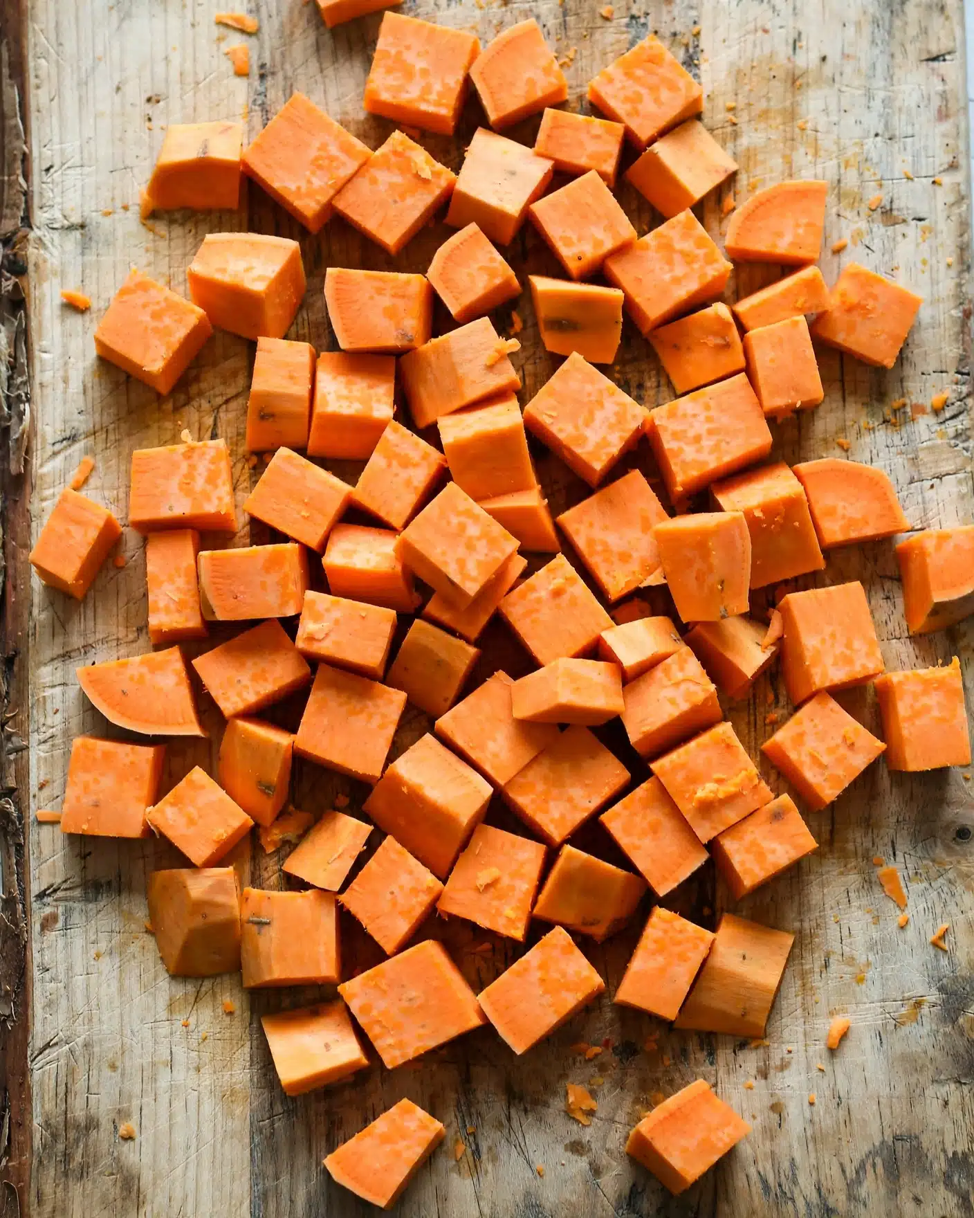 Ground Beef & Sweet Potato Burger Bowl Recipe 4 This image shows many small orange cubes of peeled sweet potato on a wooden cutting board. The pieces are uneven but mostly square or rectangular, giving a rough texture to the image. The sweet potato pieces vary slightly in size and are scattered, filling the board's surface. Photo taken with an iphone --ar 4:5 --v 7