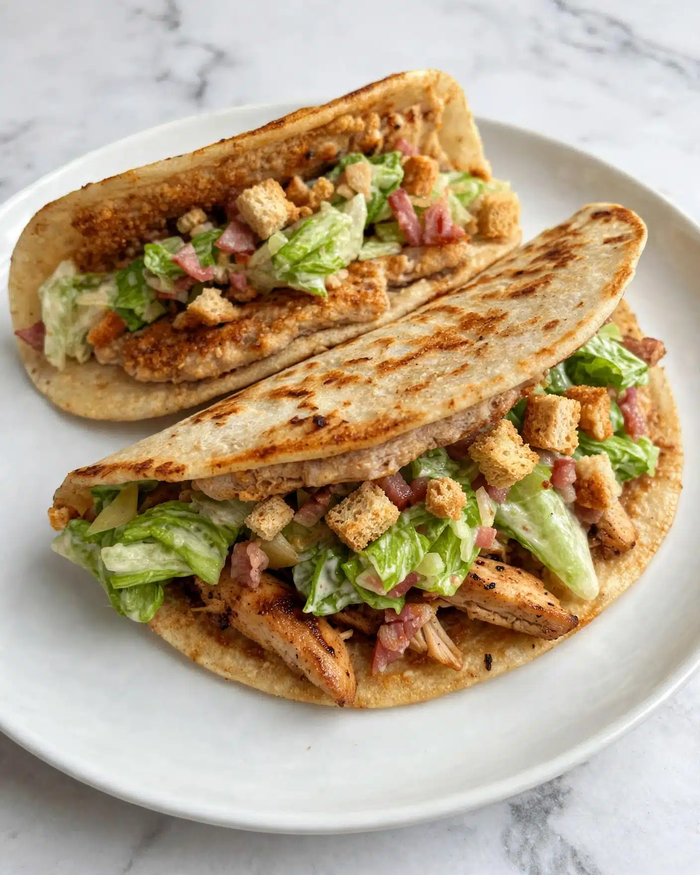 Two folded soft corn tortillas with a light golden toasted texture make the base layer on a white plate. Inside each tortilla, there is a layer of slightly browned grilled chicken, topped generously with fresh green lettuce mixed with small bits of pink bacon and crunchy light brown croutons. The textures show a mix of crispy and soft, with the colors ranging from warm beige to vibrant green and pink, all against a white marbled surface background. Photo taken with an iphone --ar 4:5 --v 7