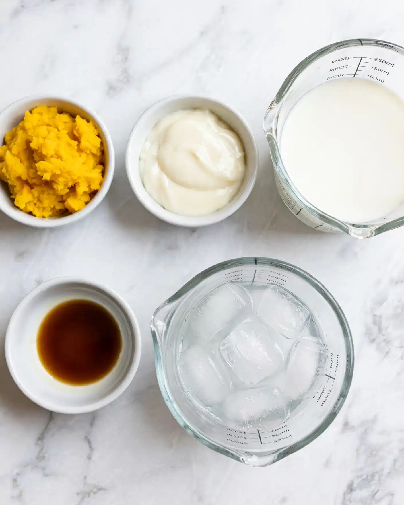 Five small bowls and a measuring cup are arranged on a white marbled surface. The top left bowl holds mashed bright yellow pumpkin with a soft and slightly chunky texture. In the center at the top is a small bowl with thick off-white condensed milk. To the right, a clear glass measuring cup contains fresh white milk. Below in the center, there is a clear glass measuring cup filled with several ice cubes that are translucent and slightly shiny. On the bottom left, a small round bowl shows a small amount of dark amber vanilla extract. The arrangement is neat and evenly spaced. Photo taken with an iphone --ar 4:5 --v 7