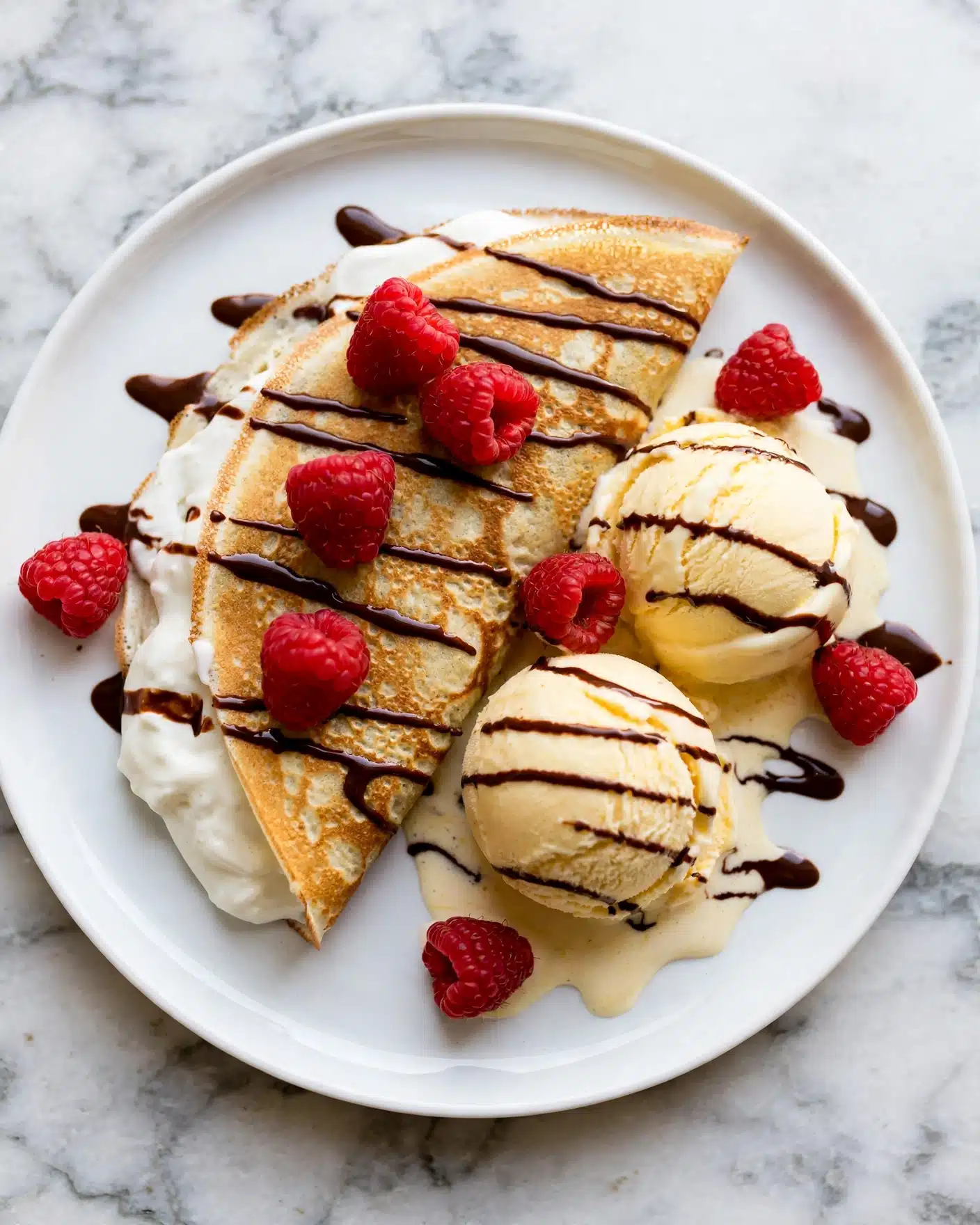 A white plate with a golden brown crepe folded in half, filled with white cream that peeks out from the edges. Two scoops of pale yellow ice cream sit beside the crepe, slightly melting. Bright red raspberries are scattered on the plate and on the crepe, adding vibrant color. Dark brown chocolate sauce is drizzled over the crepe, ice cream, and plate in thin lines. The plate sits on a white marbled surface. photo taken with an iphone --ar 4:5 --v 7