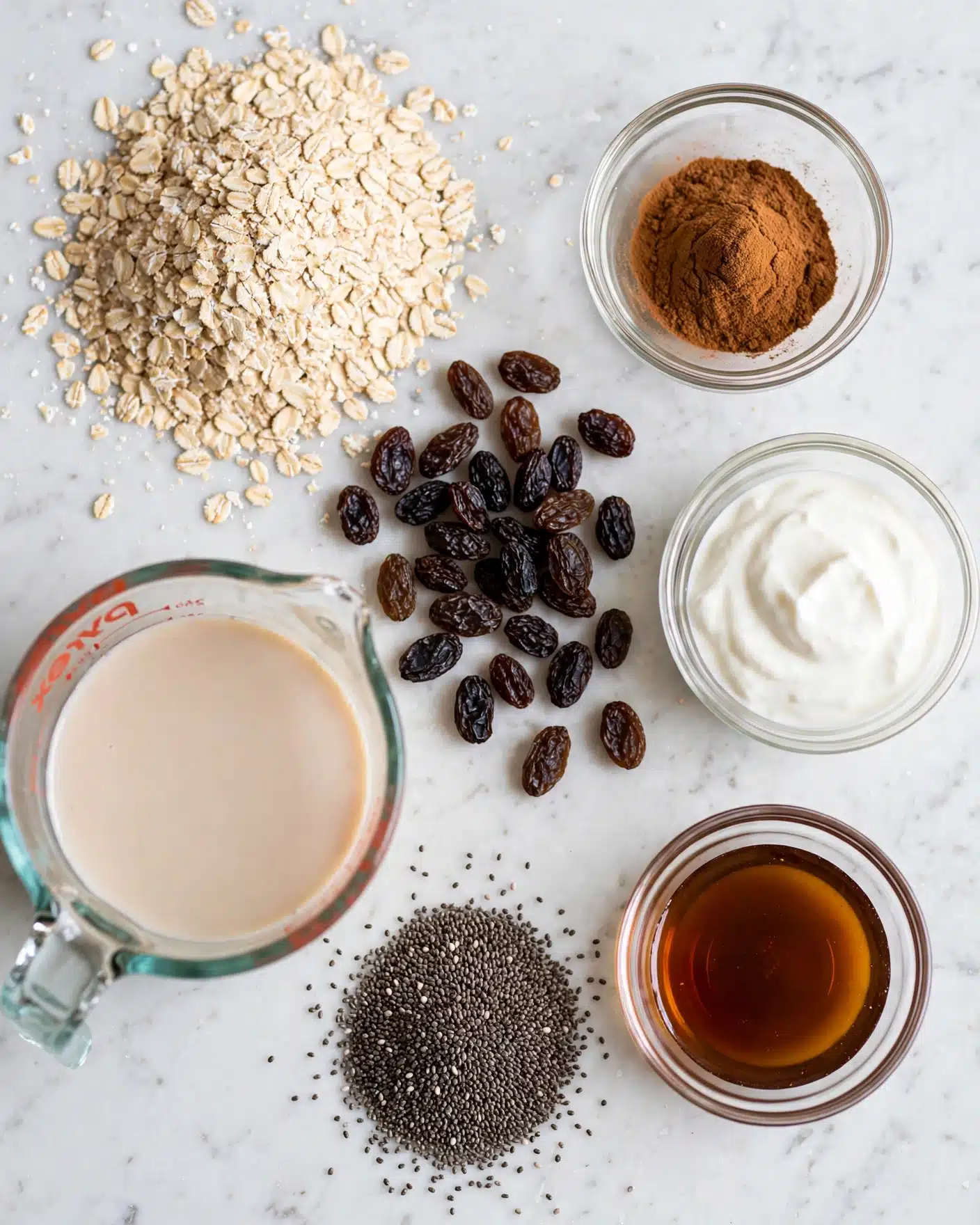 The image shows an overhead view of six ingredients spread out on a white marbled surface. Starting from the top left, there is a pile of light beige rolled oats with a rough texture. To its right, a small clear glass bowl holding a mound of dark brown cinnamon powder. Below that, another clear glass bowl contains a white creamy substance, textured softly. Moving down, a cluster of dark, wrinkled raisins is scattered roughly in the center. Near the bottom left, there is a clear measuring cup with a light beige liquid inside. Finally, at the bottom center, a heap of small black chia seeds sits next to a small clear glass bowl with a dark amber liquid inside. photo taken with an iphone --ar 4:5 --v 7