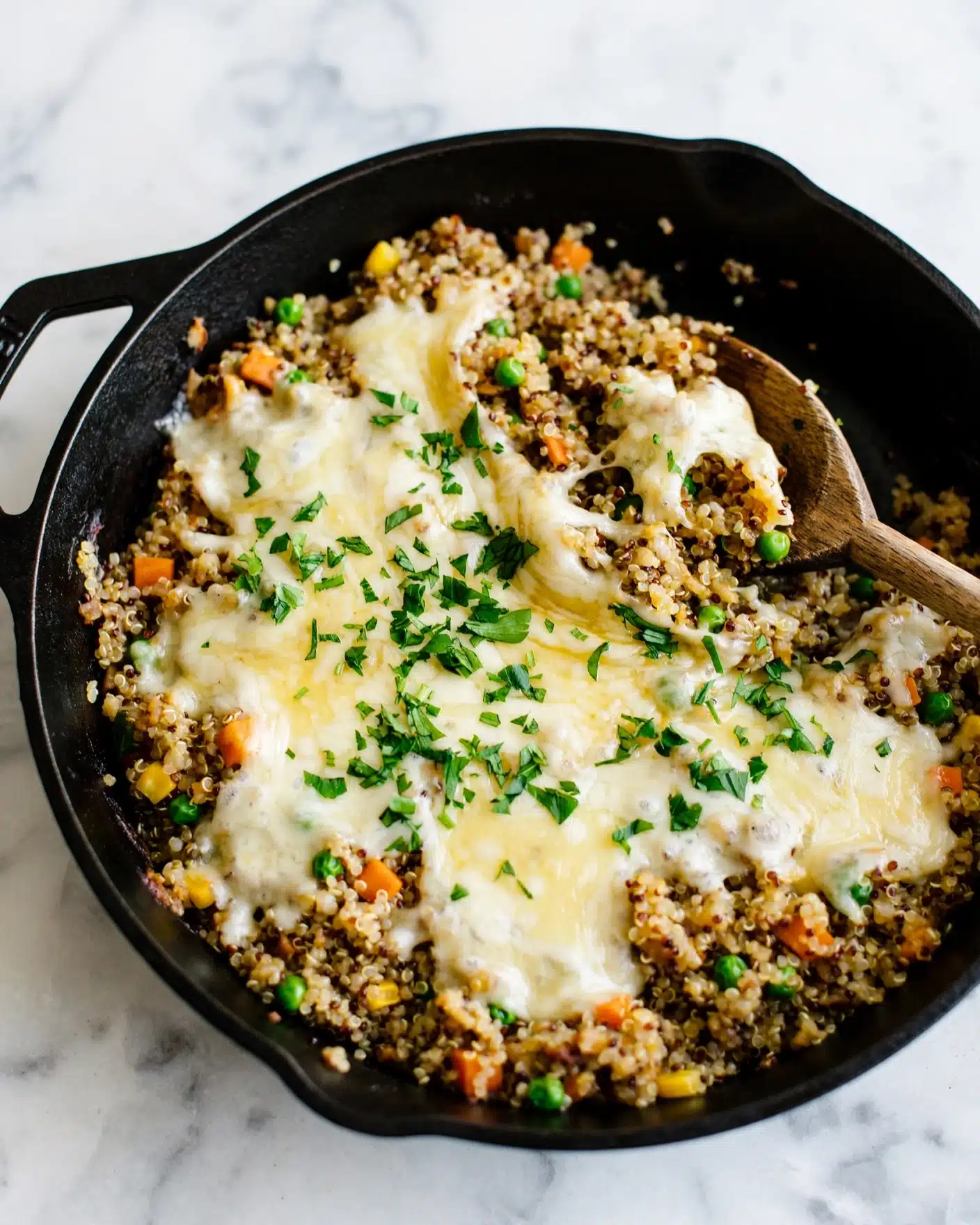 The image shows a black pan filled with a mixed dish made of grain and small vegetables in the bottom layer, with a topping of melted white and light yellow cheese spread unevenly across the middle. Bright green chopped herbs are sprinkled on top of the cheese, adding a fresh touch. There is a wooden spoon resting inside the pan, scooping some of the dish. The background is a white marbled surface. Photo taken with an iphone --ar 4:5 --v 7